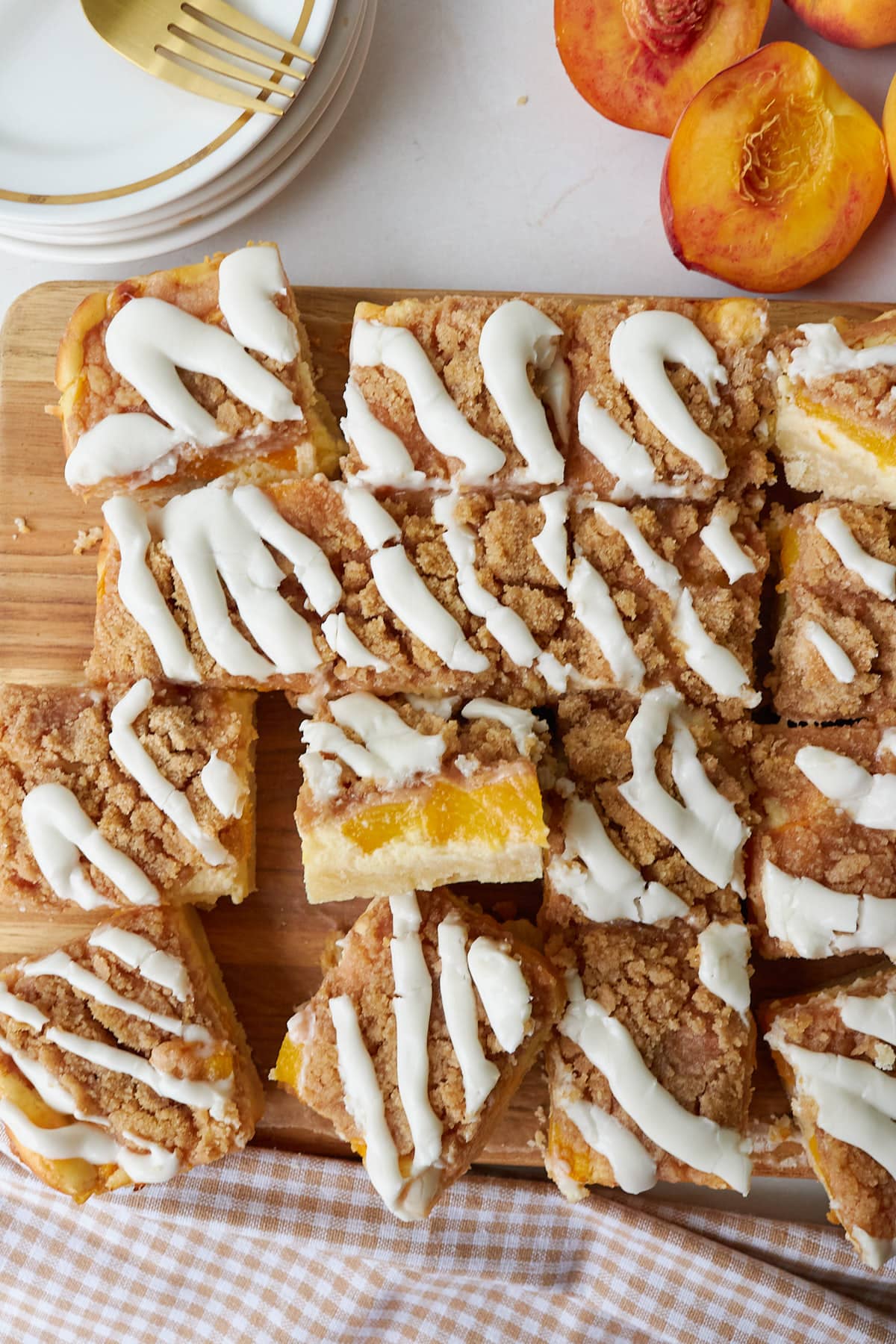 Sliced Sourdough Peach Crumble Cheesecake Bars on a wooden cutting board next to fresh peaches.