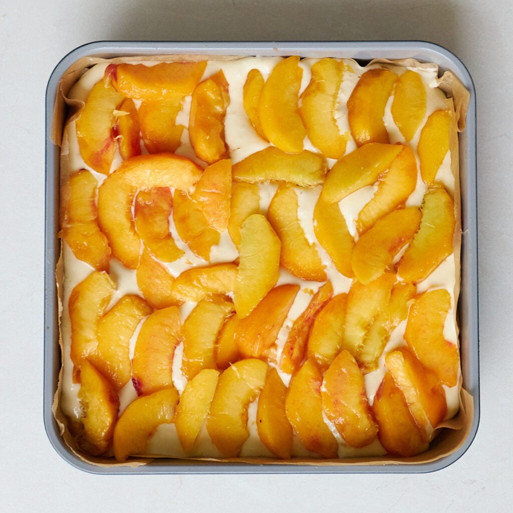 Peach layer added to a lined 9x9 pan for Sourdough Peach Crumble Cheesecake Bars.