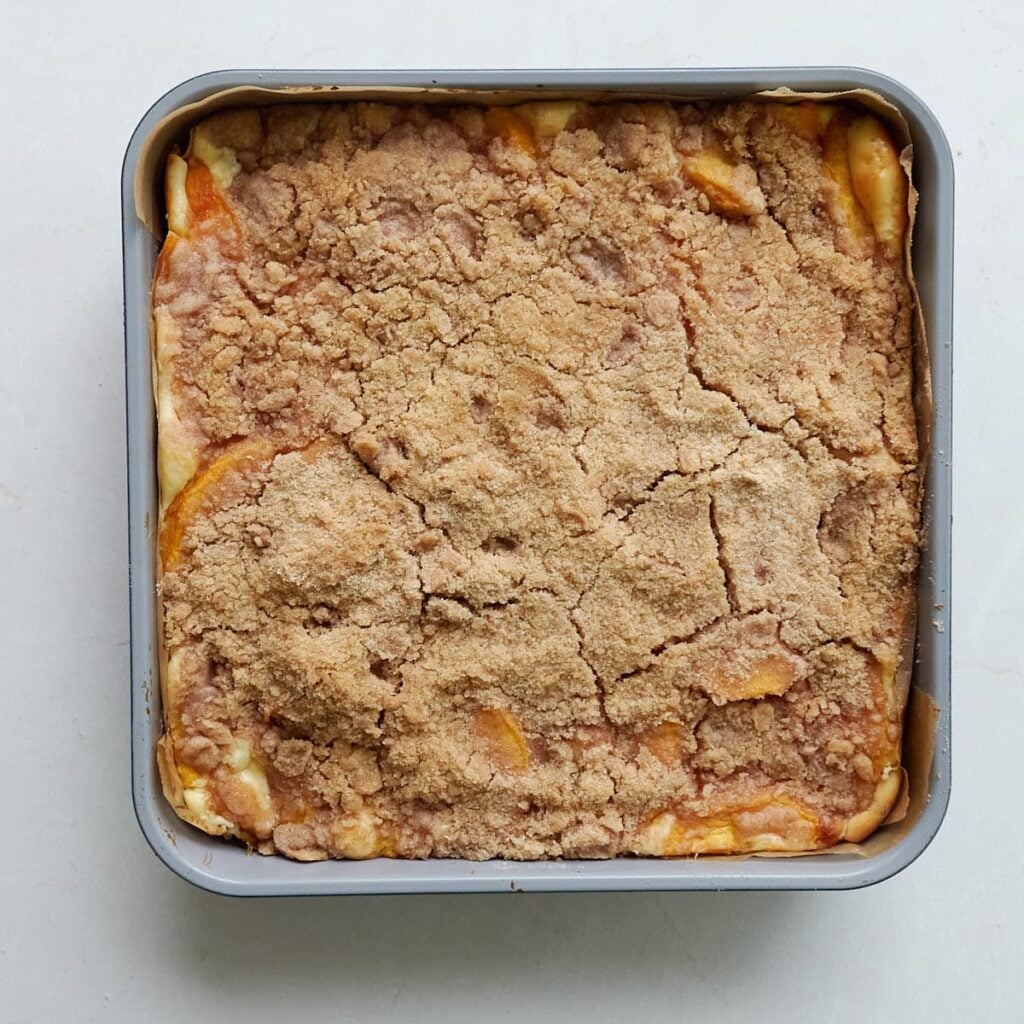Freshly baked Sourdough Peach Crumble Cheesecake Bars in a parchment paper lined 9x9 baking pan.