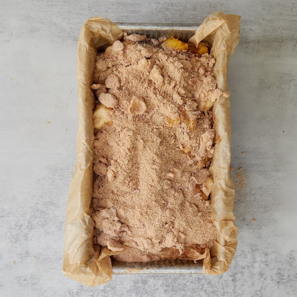 Sourdough Peach Pull-Apart Bread in a loaf pan lined with parchment paper with streusel topping added on top.
