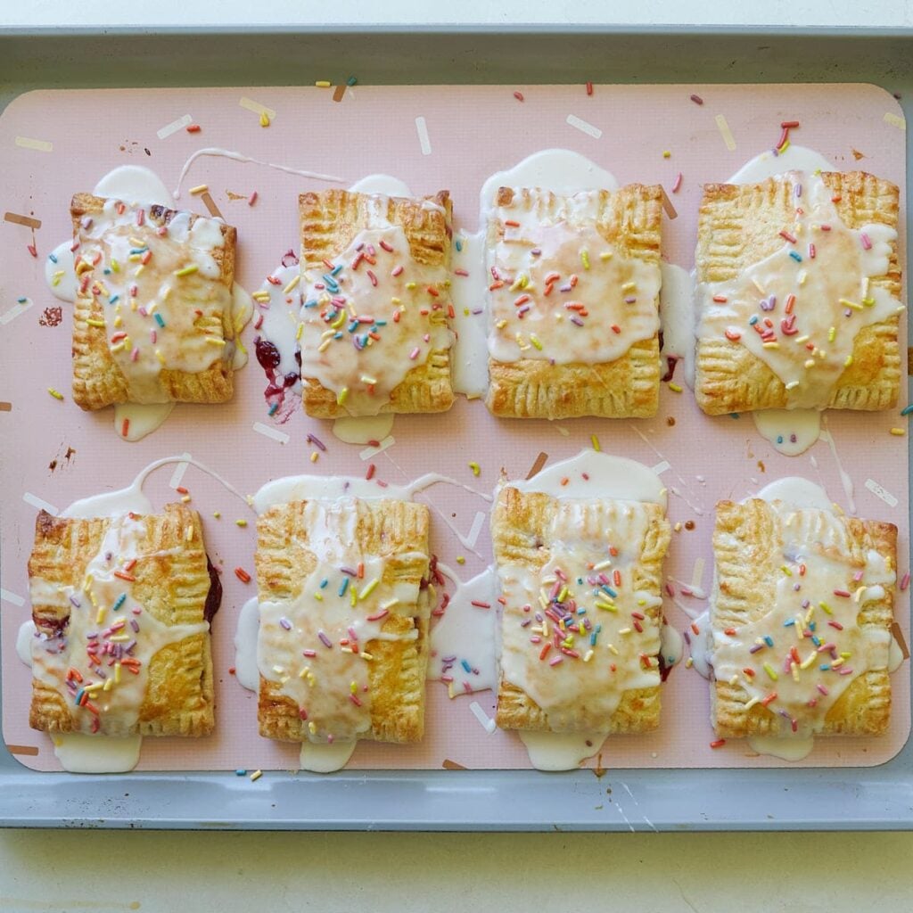 Icing and sprinkles added to Sourdough Pop Tarts on a sheet pan lined with a silicone baking mat.