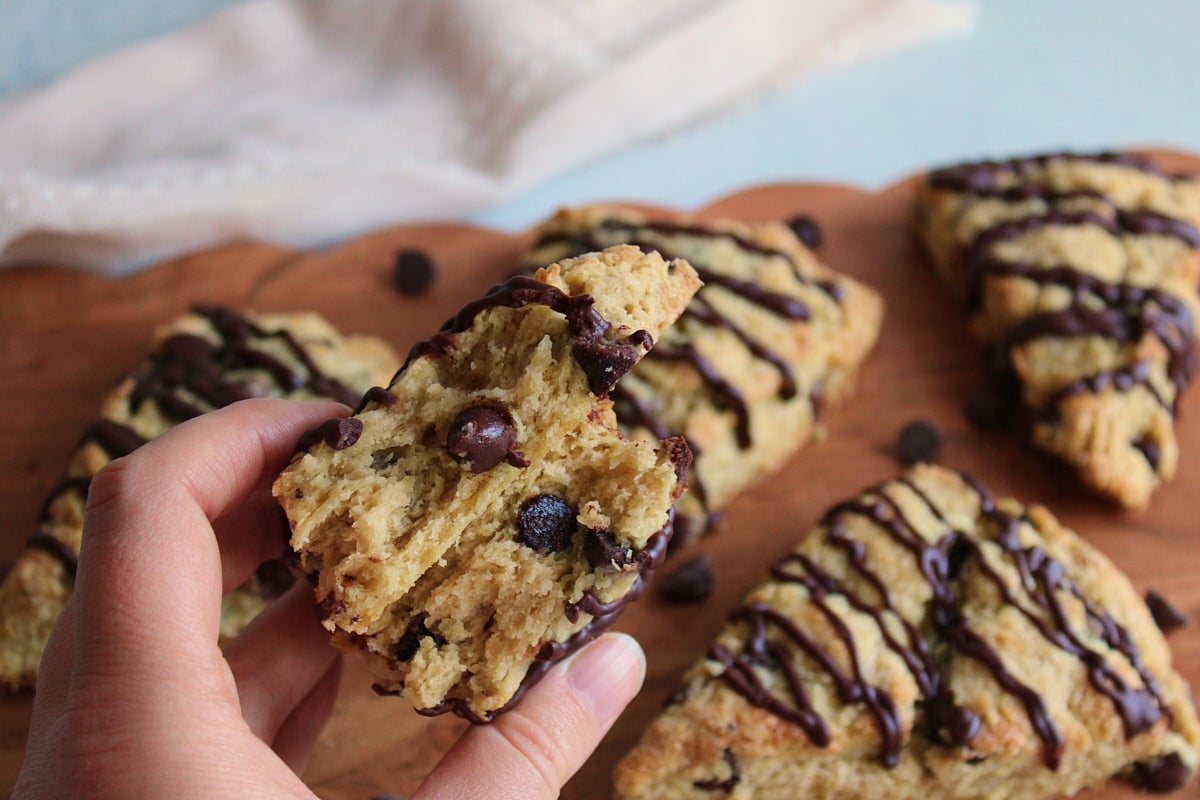 A hand holding a Chocolate Chip Sourdough Scone over a wooden cutting board.
