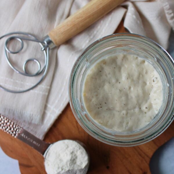 Sourdough starter in a jar next to a measuring cup of flour and a danish dough whisk.