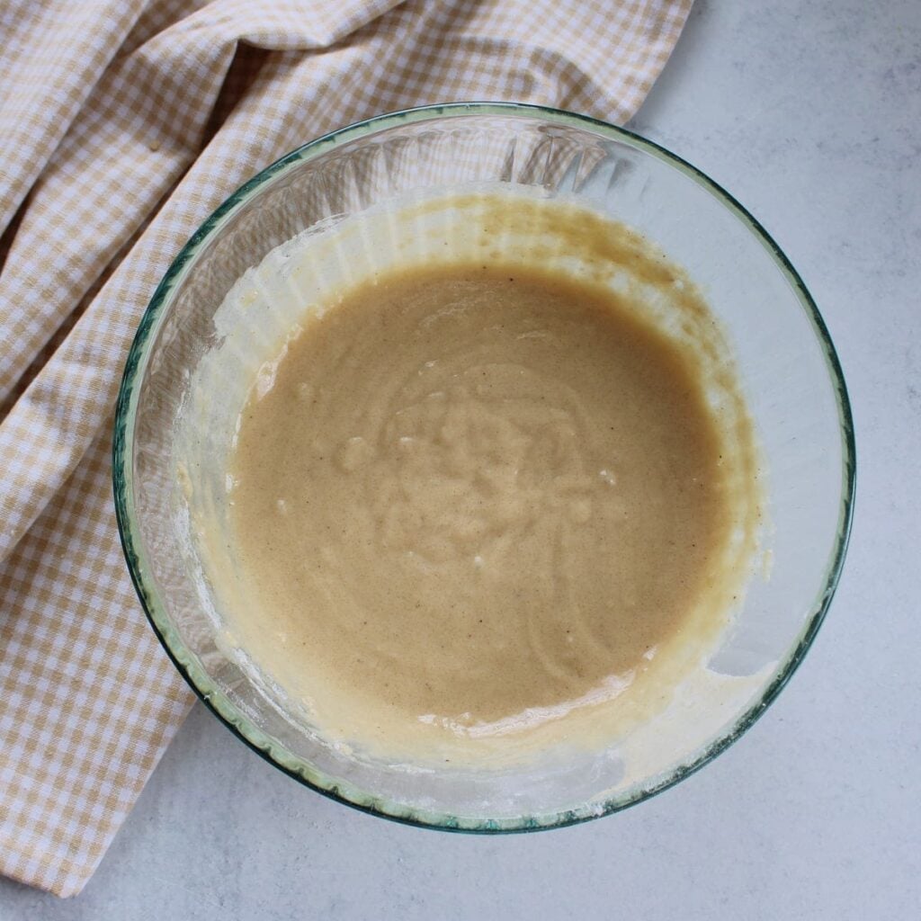 Batter for sourdough discard donuts in a clear bowl next to a brown and white cloth napkin.