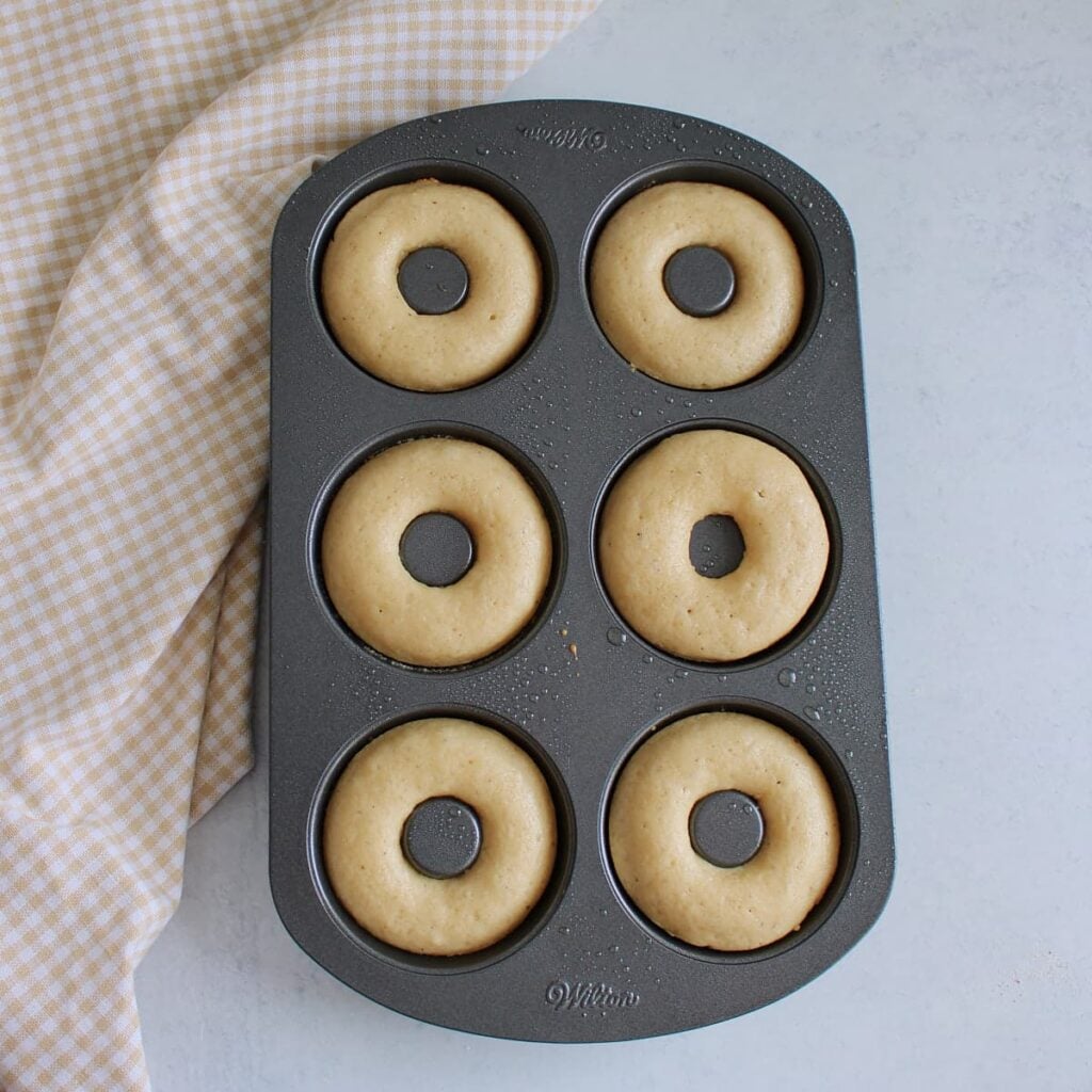 Freshly baked sourdough discard donuts in a donut pan next to a white and brown cloth napkin.