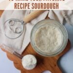 Sourdough starter in a jar next to a measuring cup of flour and a danish dough whisk.