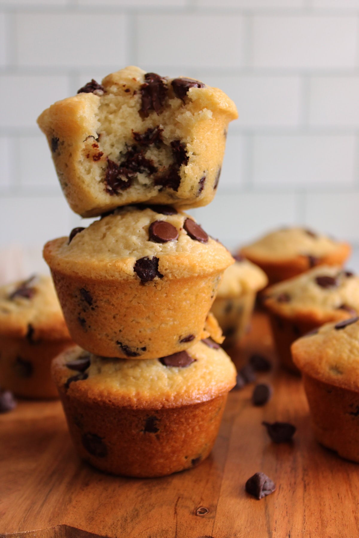 Three Chocolate Chip Sourdough Muffins stacked on top of each other on a wooden cutting board.