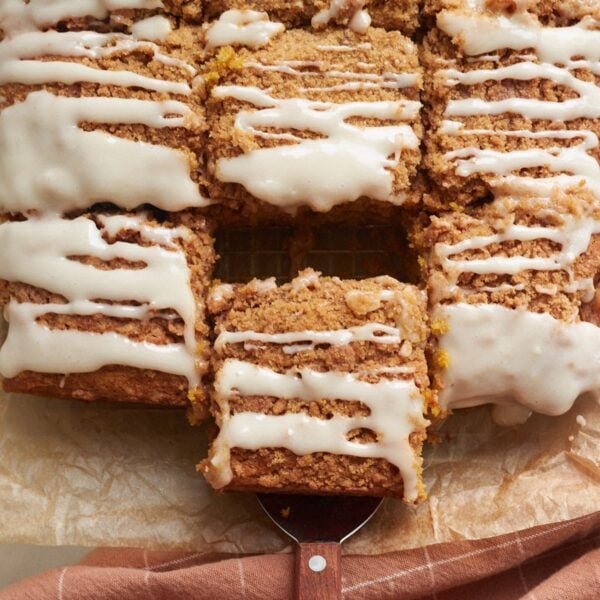 Sourdough Pumpkin Coffee Cake sliced into squares on parchment paper with a wooden handle serving spatula.