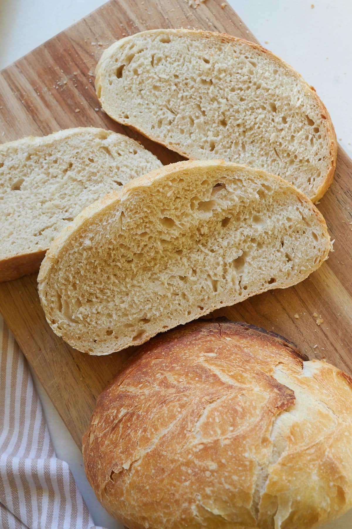 Three slices of sourdough discard bread on a cutting board next to half a loaf.