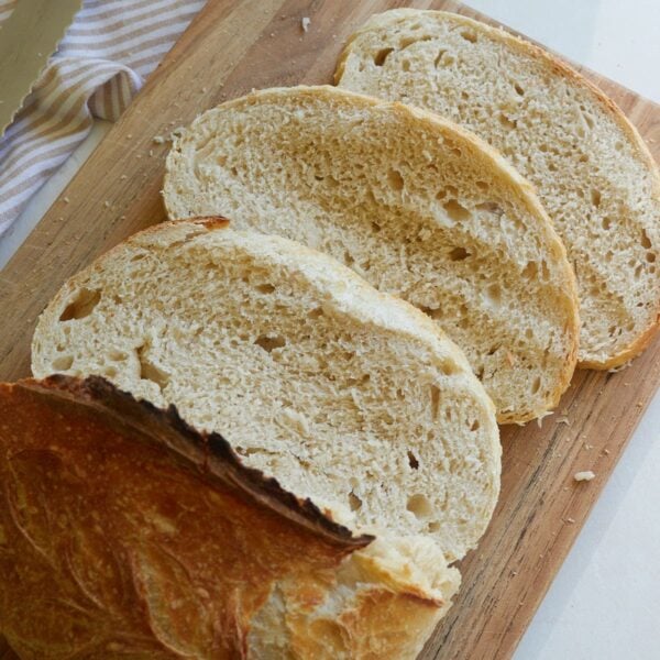 Three slices of sourdough discard bread on a cutting board next to half a loaf.