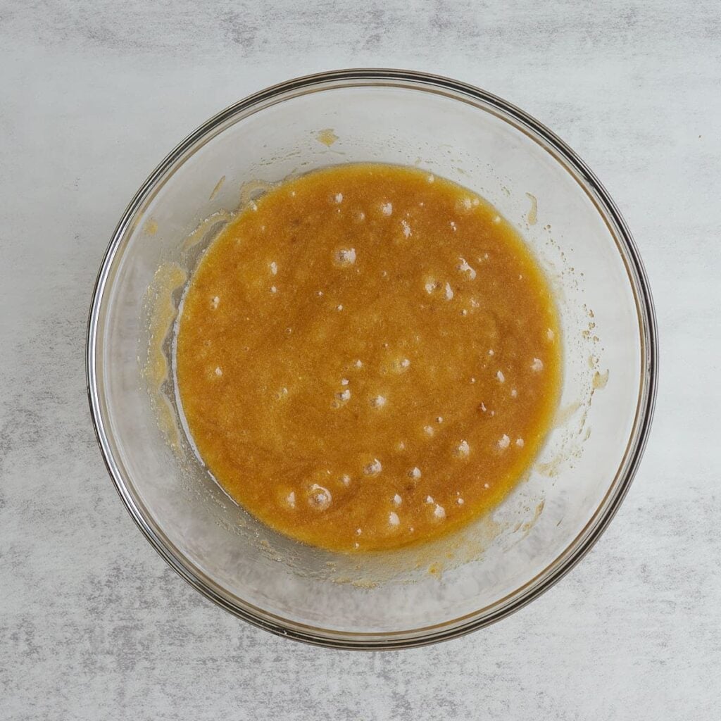 Sugar, oil, and eggs mixed together in a clear bowl for sourdough pumpkin coffee cake.