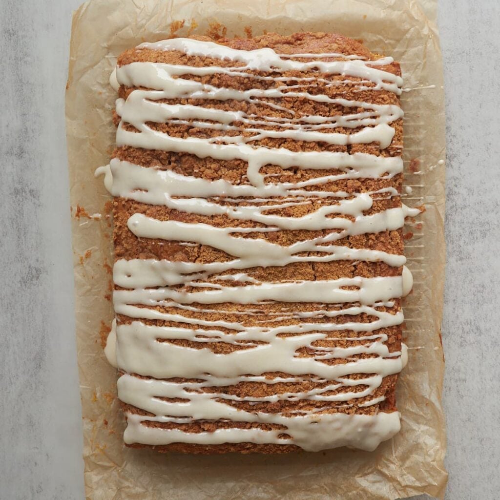 Icing drizzled on top of sourdough pumpkin coffee cake on parchment paper.