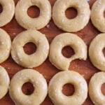 Maple Glazed Sourdough Donuts with flaky salt on top on a wooden board with the middle donut missing a bite.
