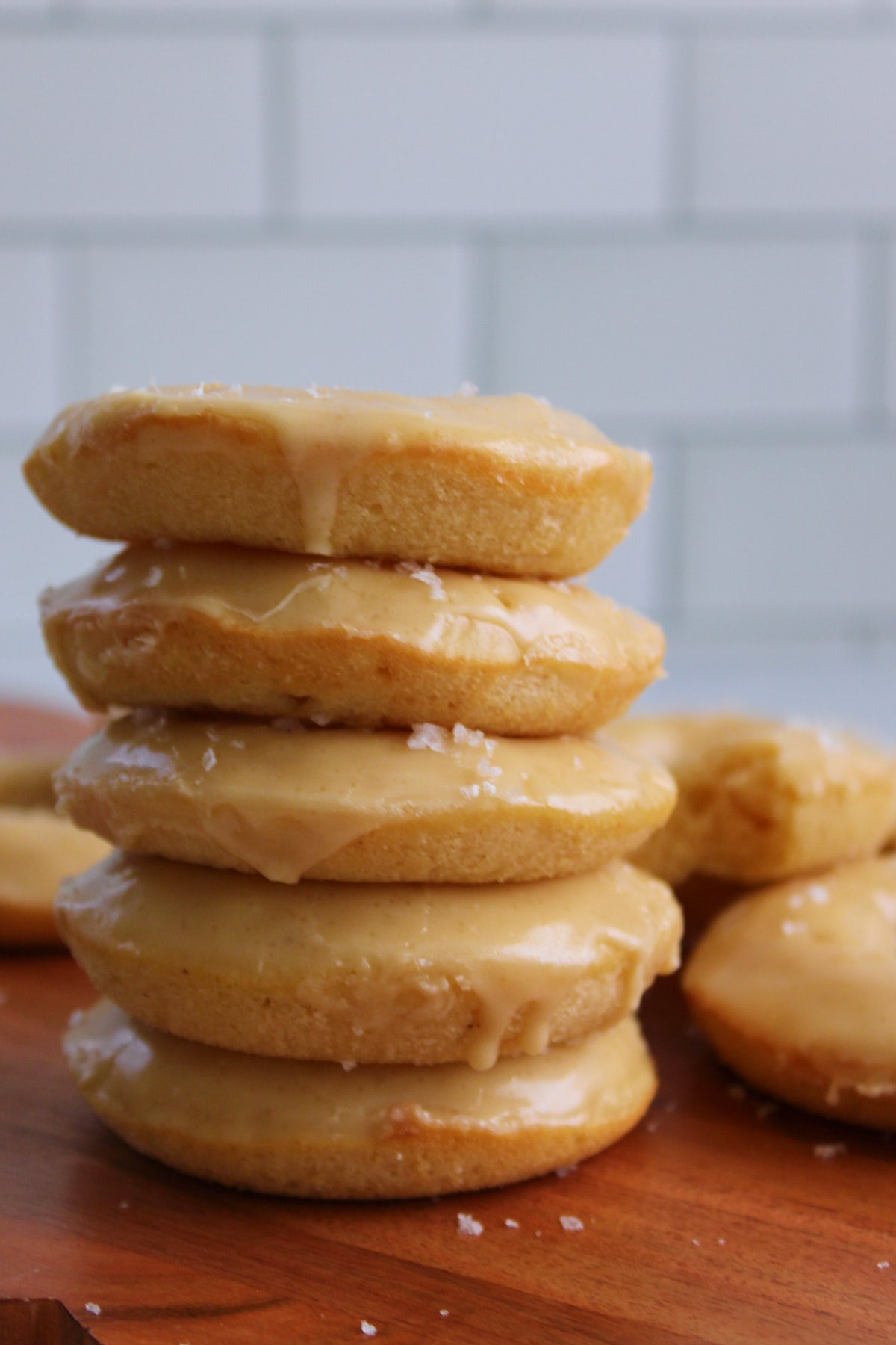 Five Maple Glazed Sourdough Donuts stacked on top of each other on a wooden board.