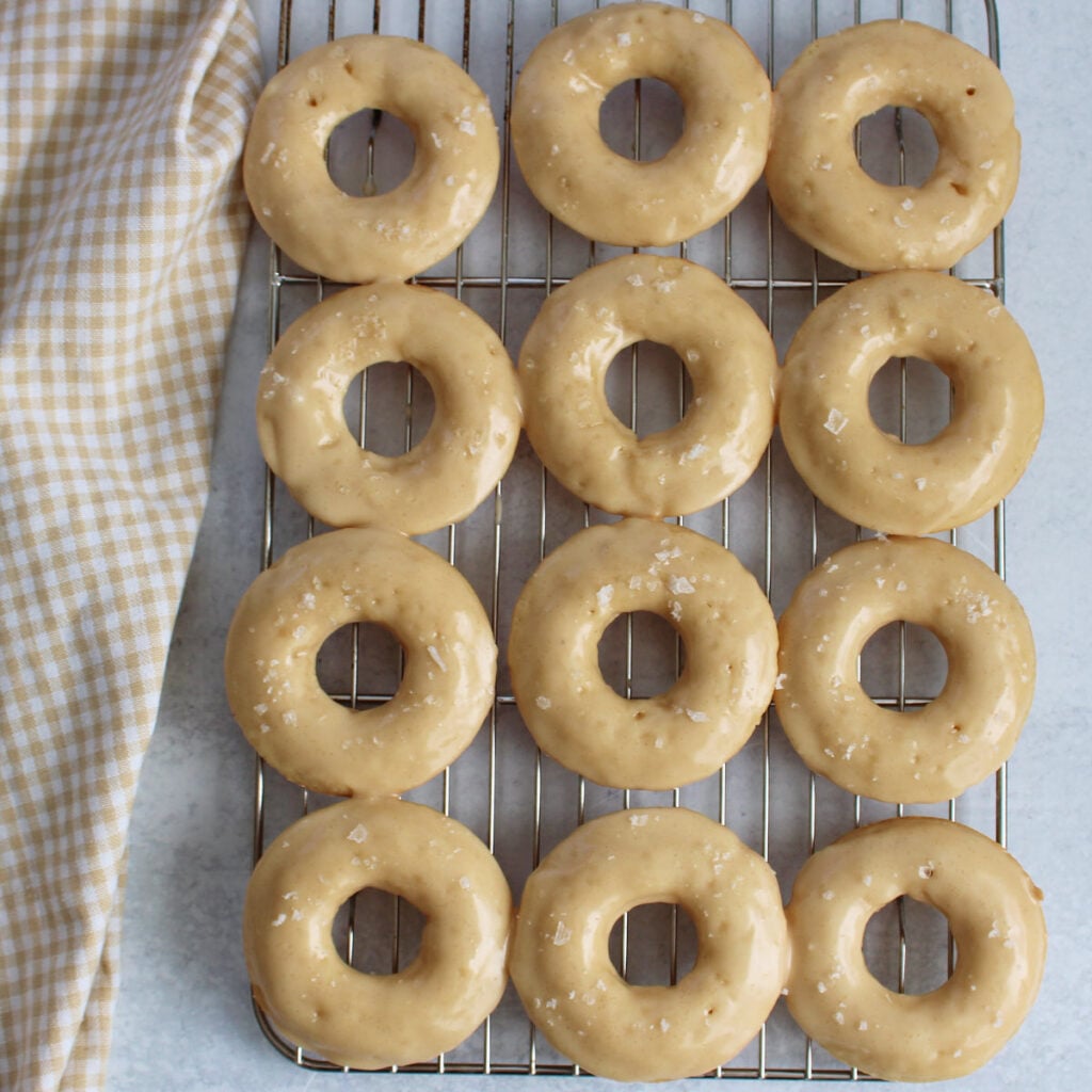 12 Maple Glazed Sourdough Donuts on a cooling rack next to a white and brown cloth napkin.
