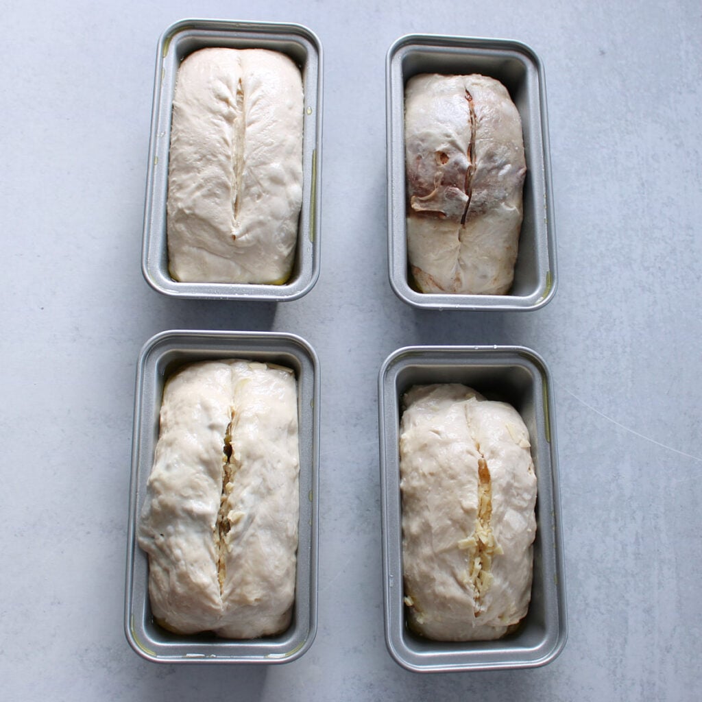 Four sourdough mini bread loaves in a mini loaf pans with a score down the middle.