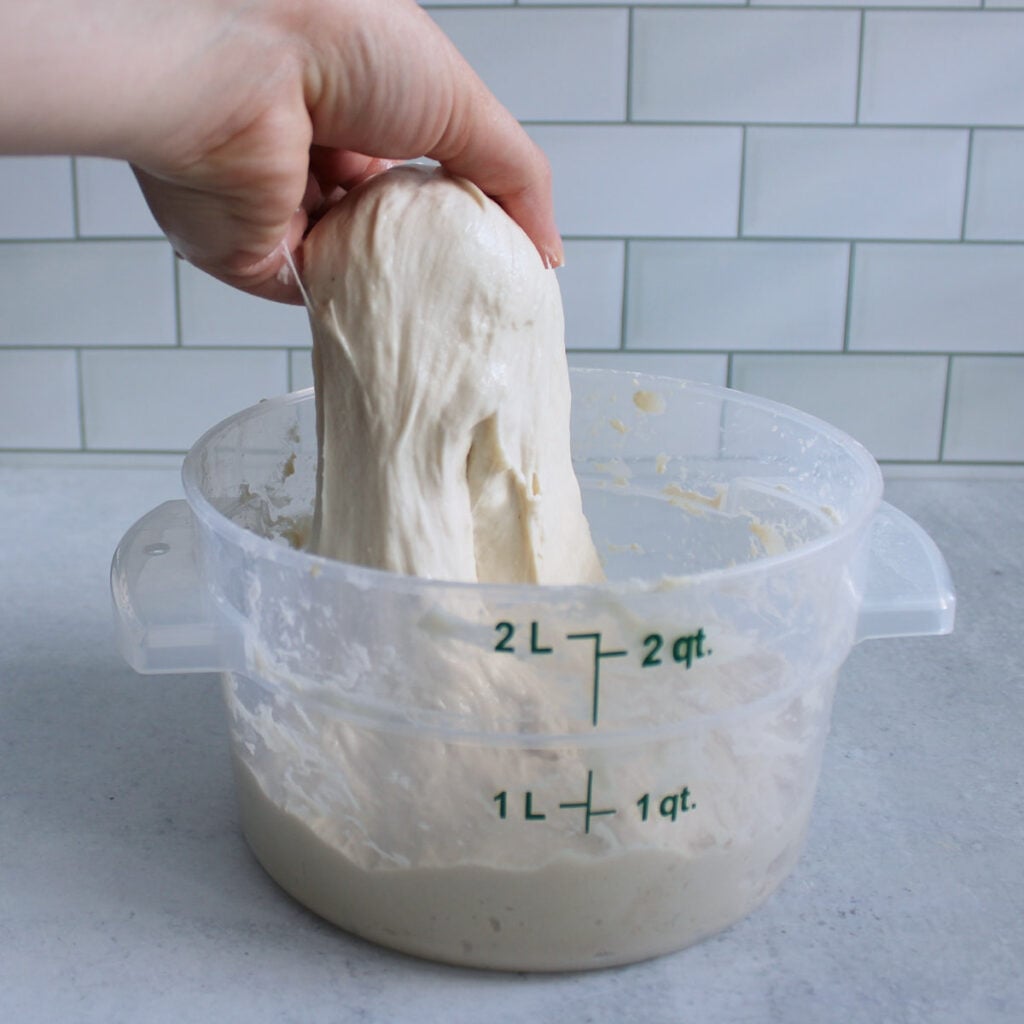 A hand pulling up the dough for sourdough mini loaves to do a set of stretch and folds.