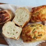 Sourdough mini loaves on a wooden board with one loaf sliced in half.
