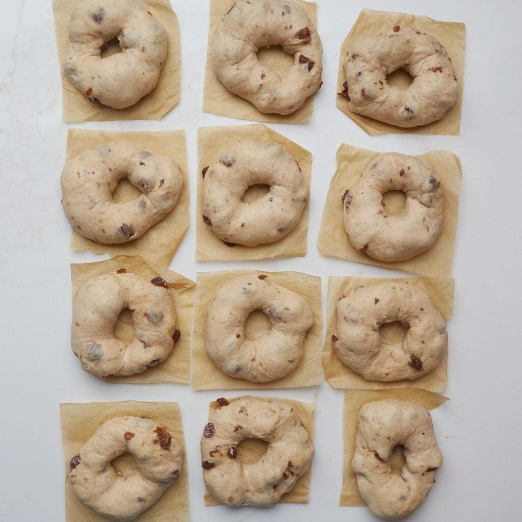 Sourdough cinnamon raisin bagels on square pieces of parchment paper.