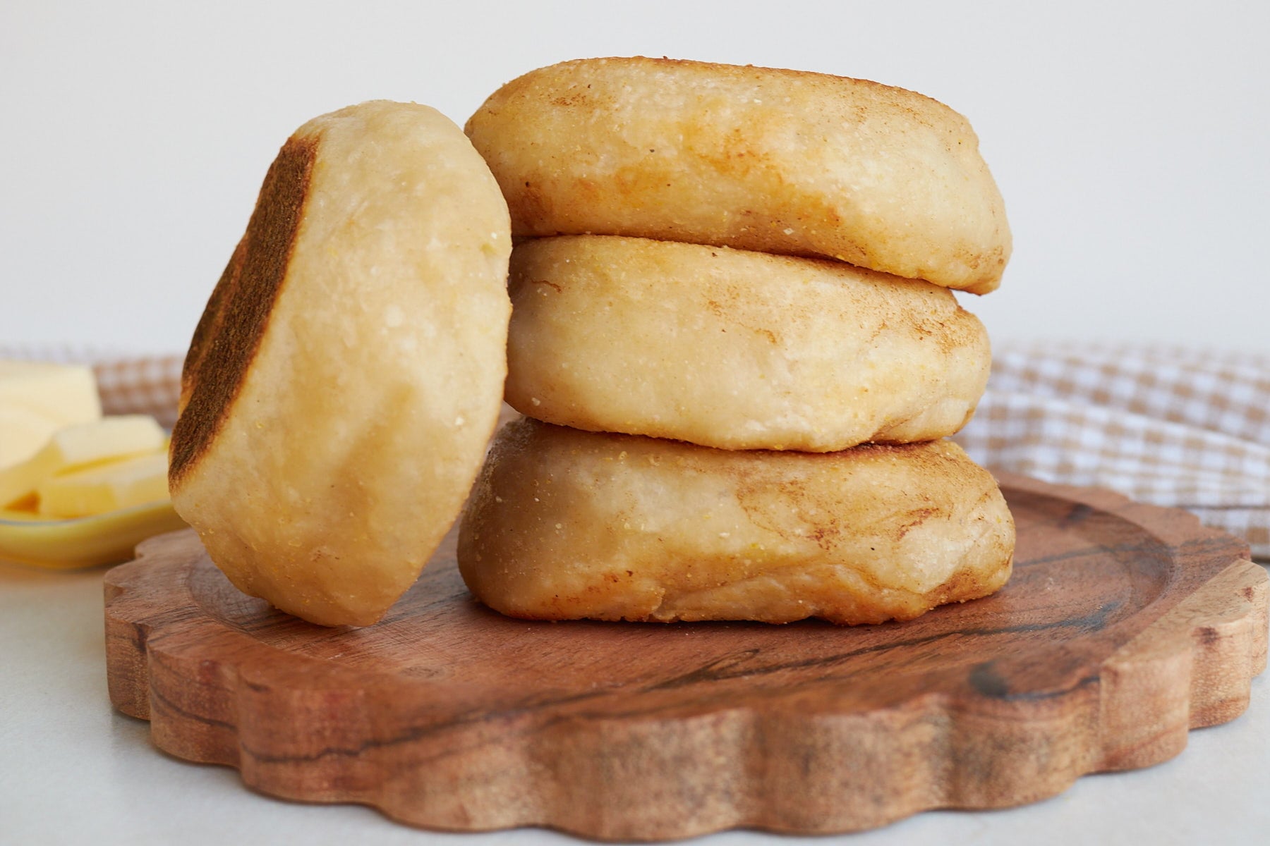 Three Sourdough English Muffins stacked on top of each other with one leaning next to it.