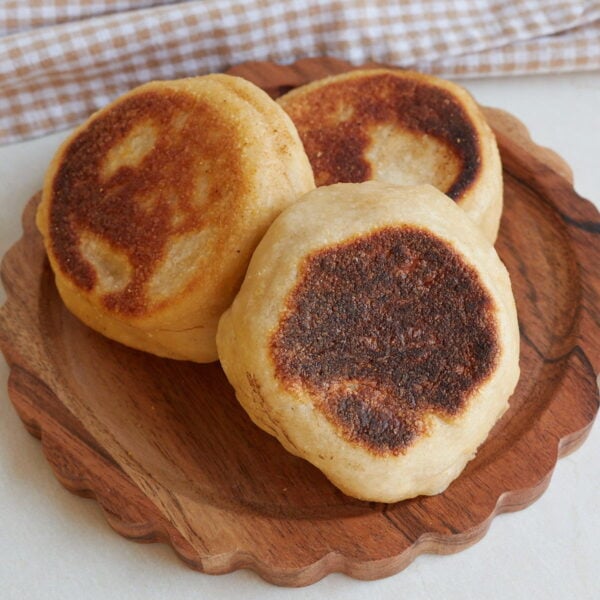 Three Sourdough English Muffins on a wooden plate.