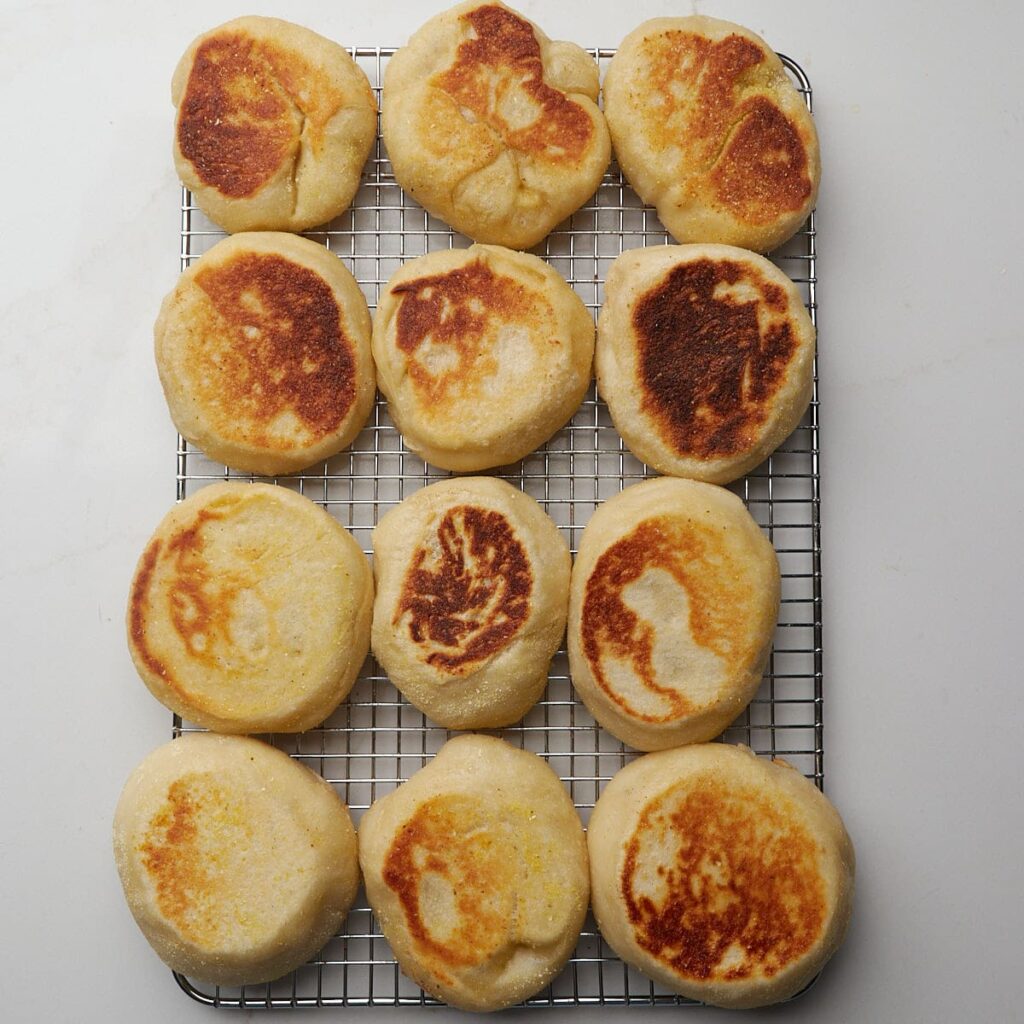12 Sourdough English Muffins freshly cooked on a wire rack.